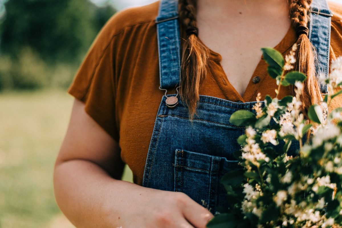 woman in brown crew neck t-shirt and blue denim dungaree holding white flowers